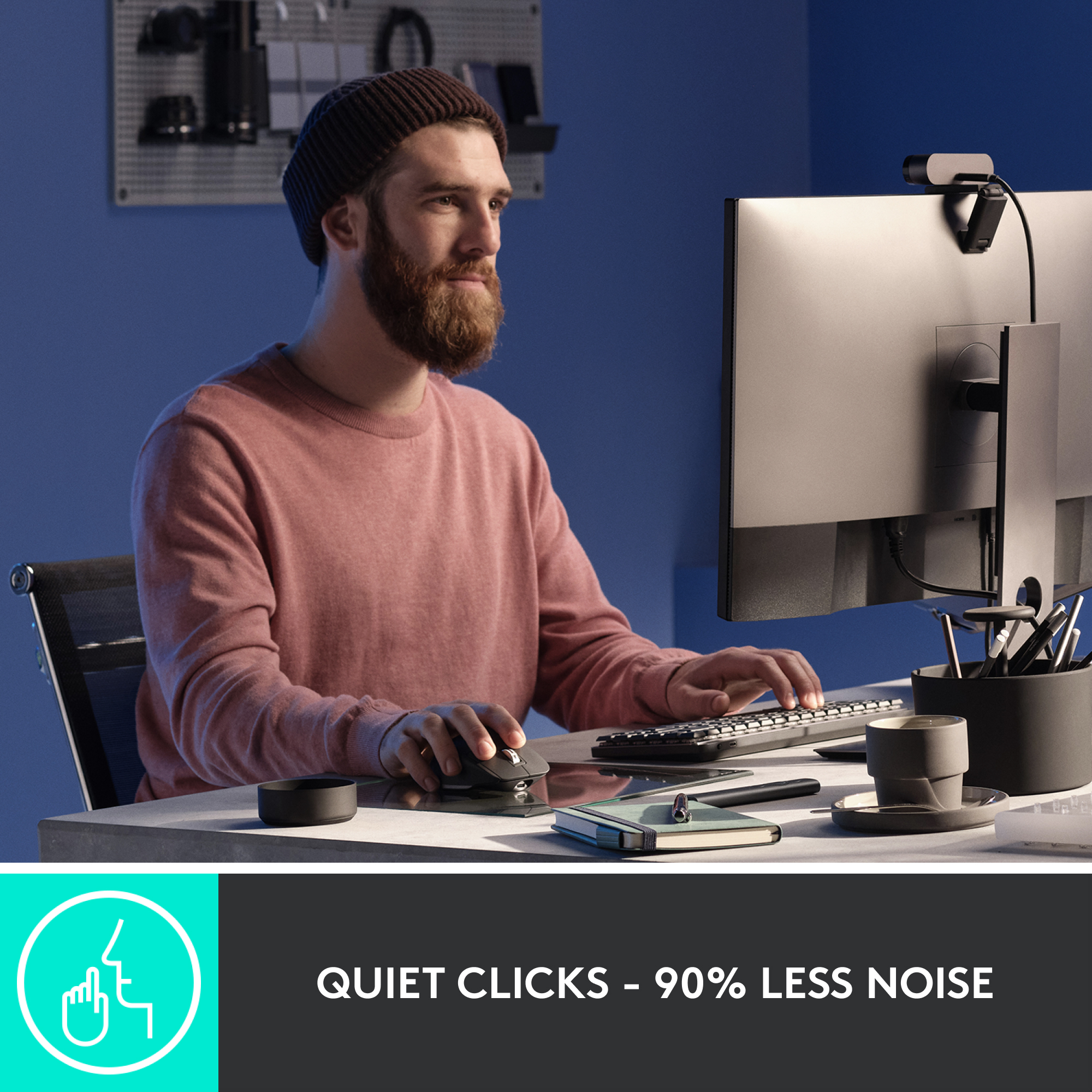 Un homme utilise une souris et un clavier. Un moniteur et une webcam sont également visibles.