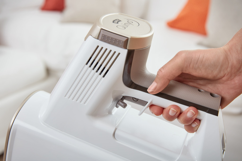 Une main tenant un aspirateur blanc et gris. L'arrière-plan est flou.