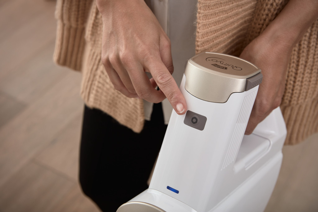 Personne appuyant sur un bouton d'un aspirateur blanc. Pull beige. Gros plan.