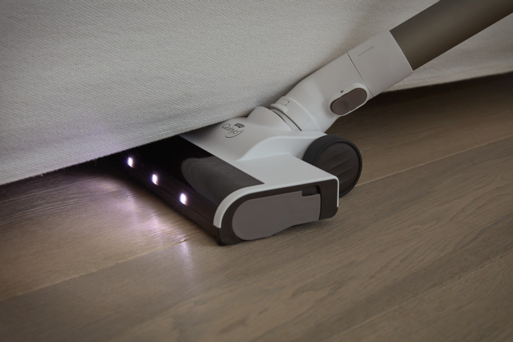 Tête d'aspirateur nettoyant sous un canapé blanc. La tête est éclairée par des lumières LED.