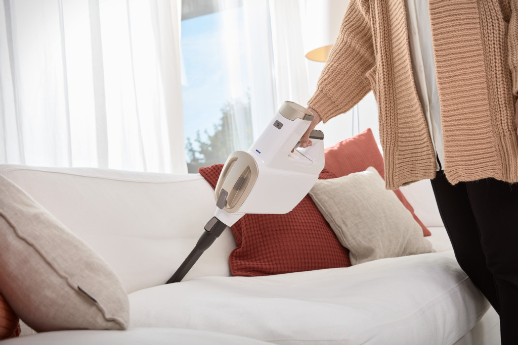 Une personne passe l'aspirateur sur un canapé blanc avec un aspirateur à main, montrant l'action.