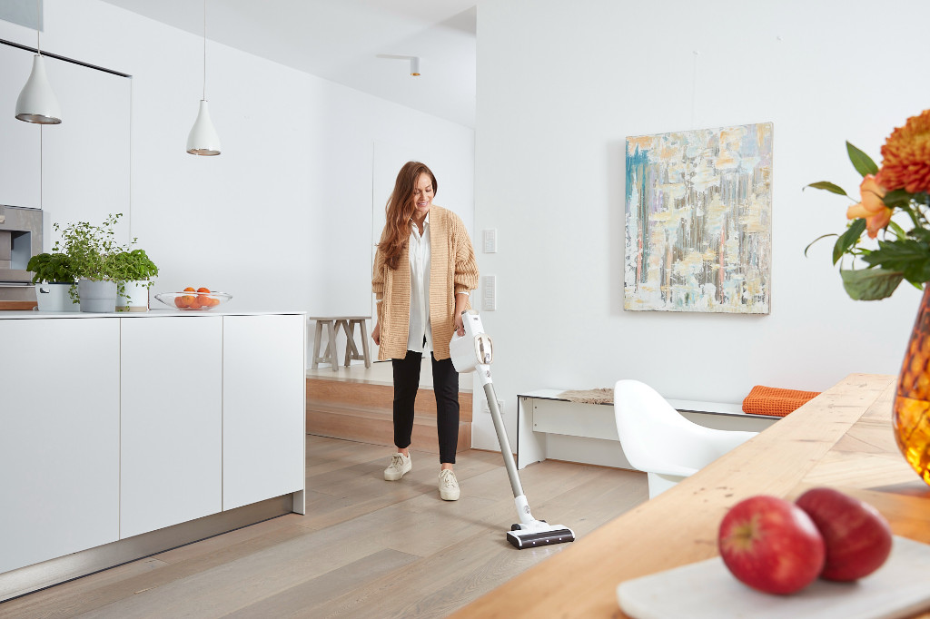 Une femme passe l'aspirateur dans une pièce. Une table en bois avec des fruits au premier plan.