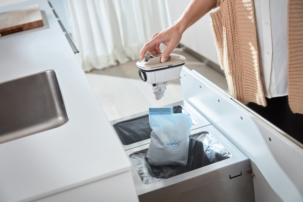 Personne plaçant un filtre dans une poubelle de cuisine. D'autres poubelles et un sac filtrant Swirl sont visibles.