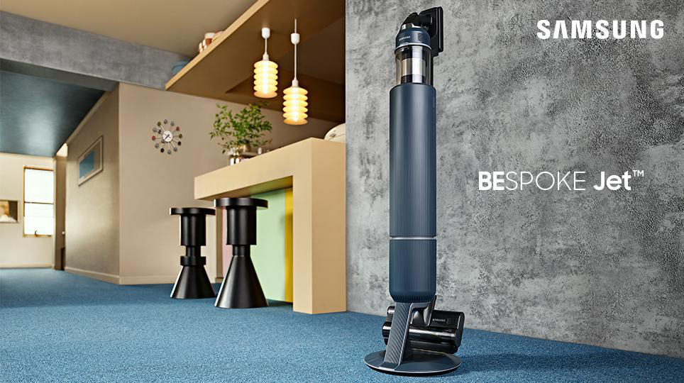 Ein modernes Interieur mit blauem Teppich, schwarzen Hockern und einem Samsung Bespoke Jet Staubsauger.
