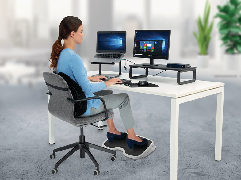 Nő asztalnál laptop, monitor és lábtartó.
