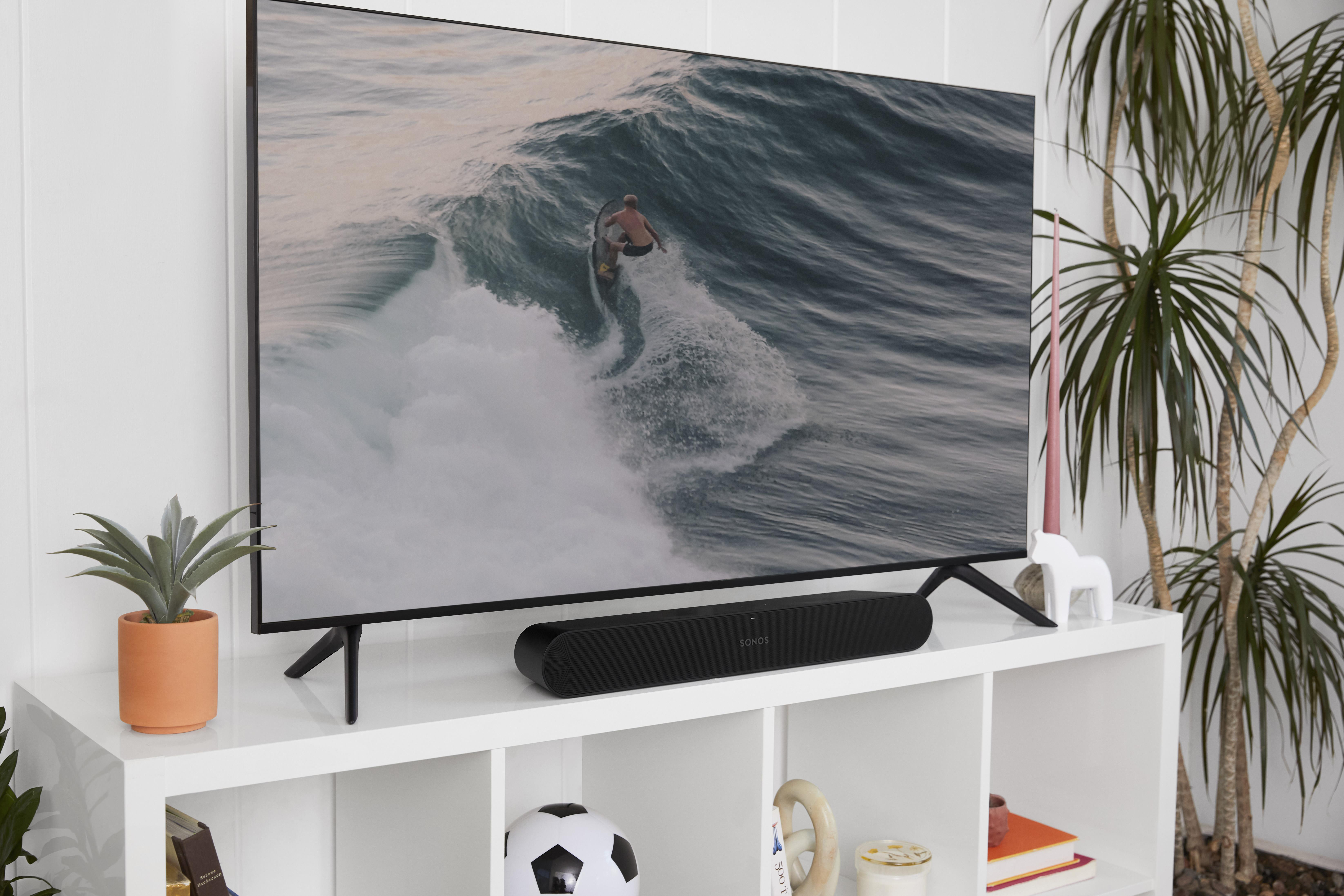 Fernseher mit Surfer auf Welle und Lautsprecher. Weißes Regal mit Deko.