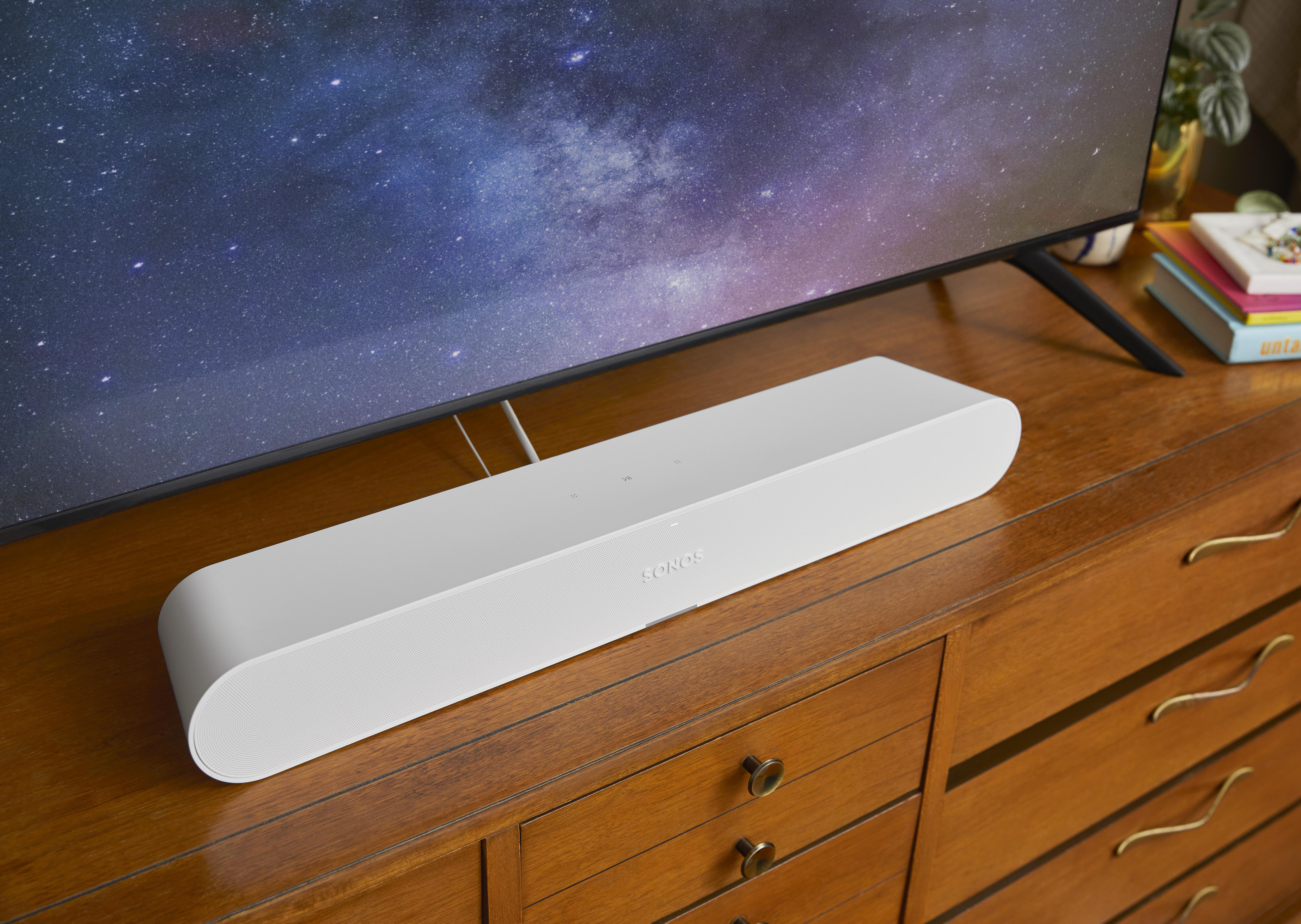 Eine weiße Soundbar auf einem Holzschrank unter einem Fernseher, mit Sternenhimmel im Hintergrund.