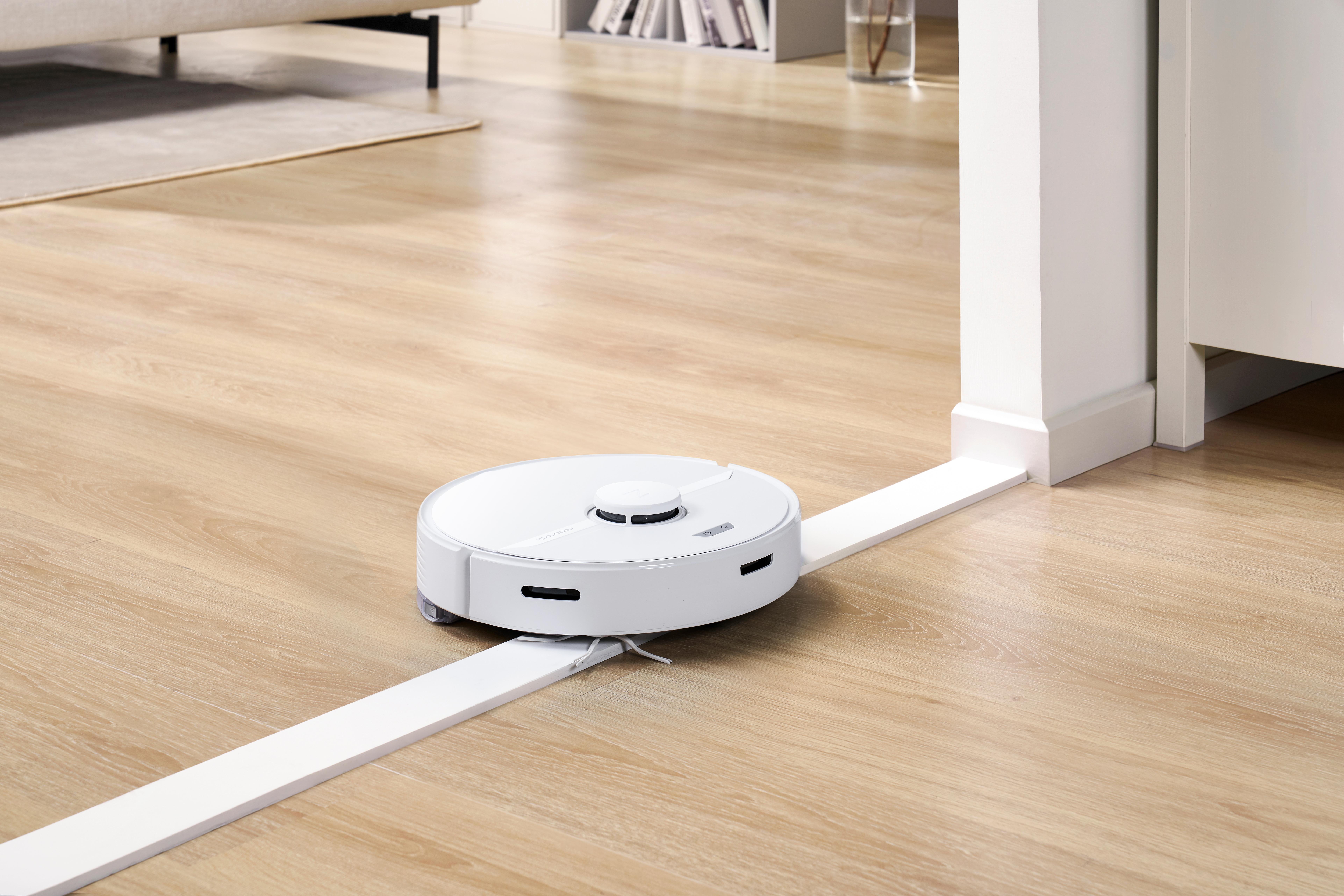 Ein Roboter-Staubsauger, der auf einem Holzfußboden entlang eines weißen Führungsstreifens fährt.