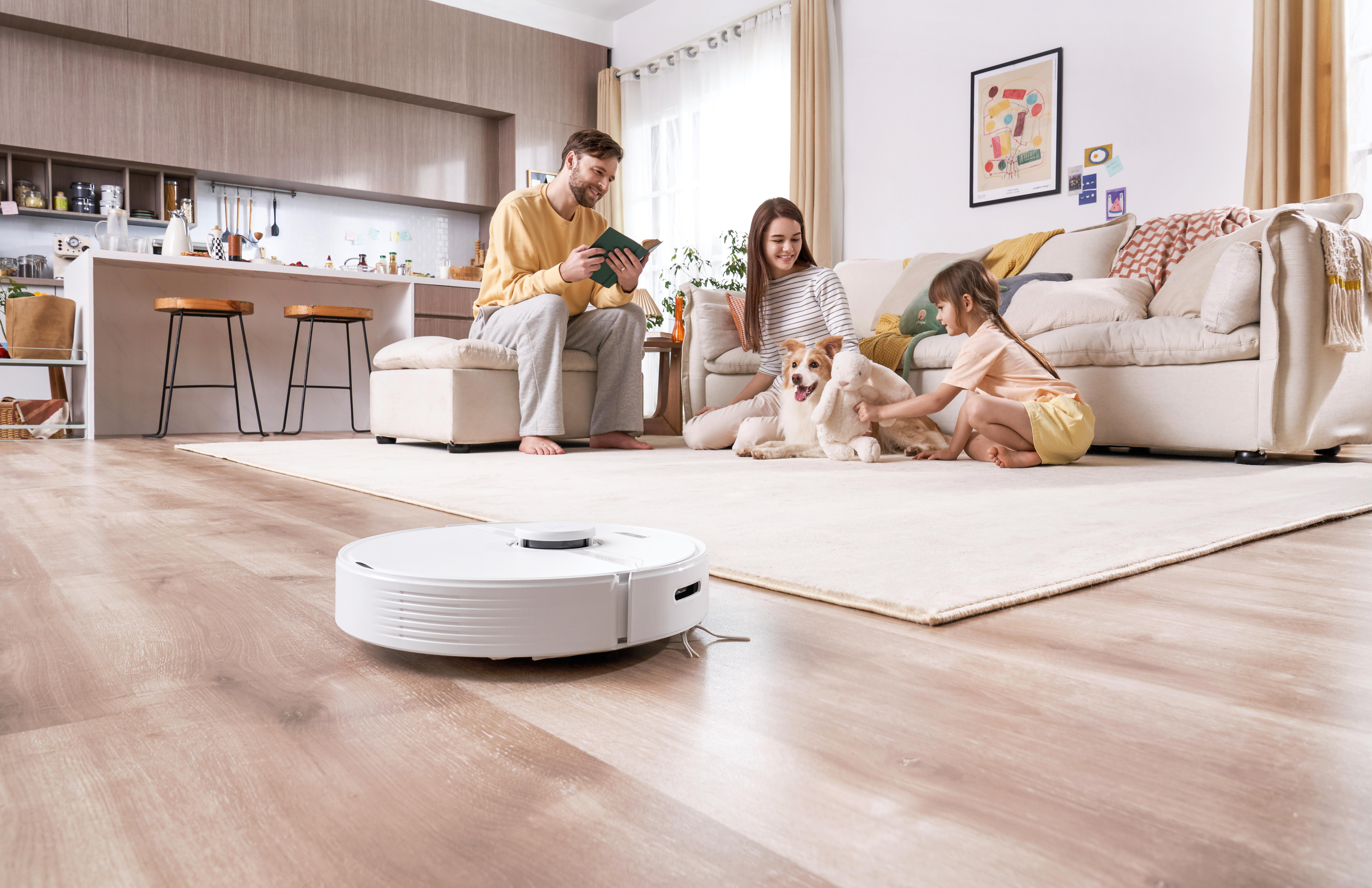 Familie im Wohnzimmer mit Roboterstaubsauger. Hund und Kind sind anwesend.