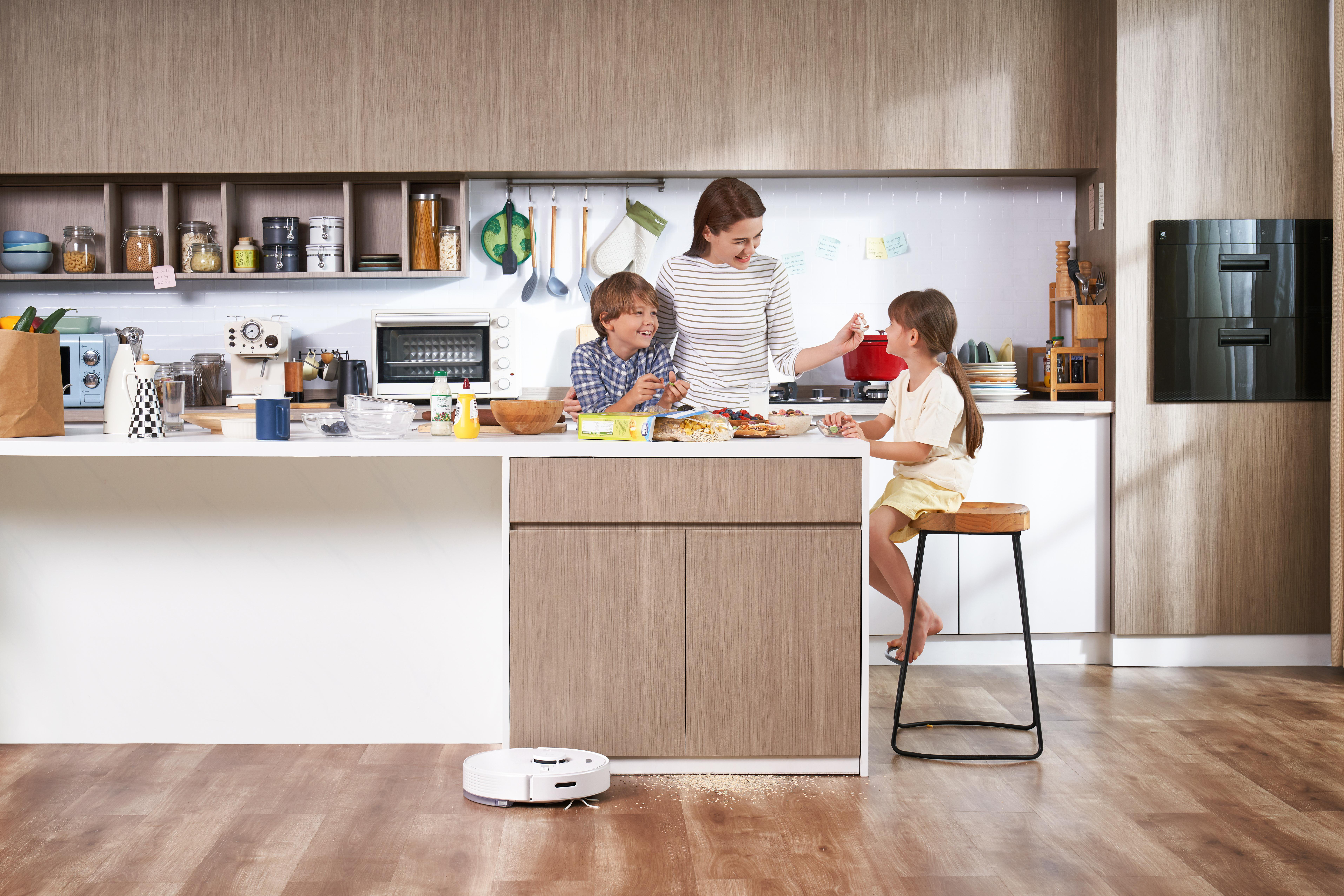 Familie kocht in der Küche. Roboter-Staubsauger reinigt den Boden. Weißer Hintergrund.