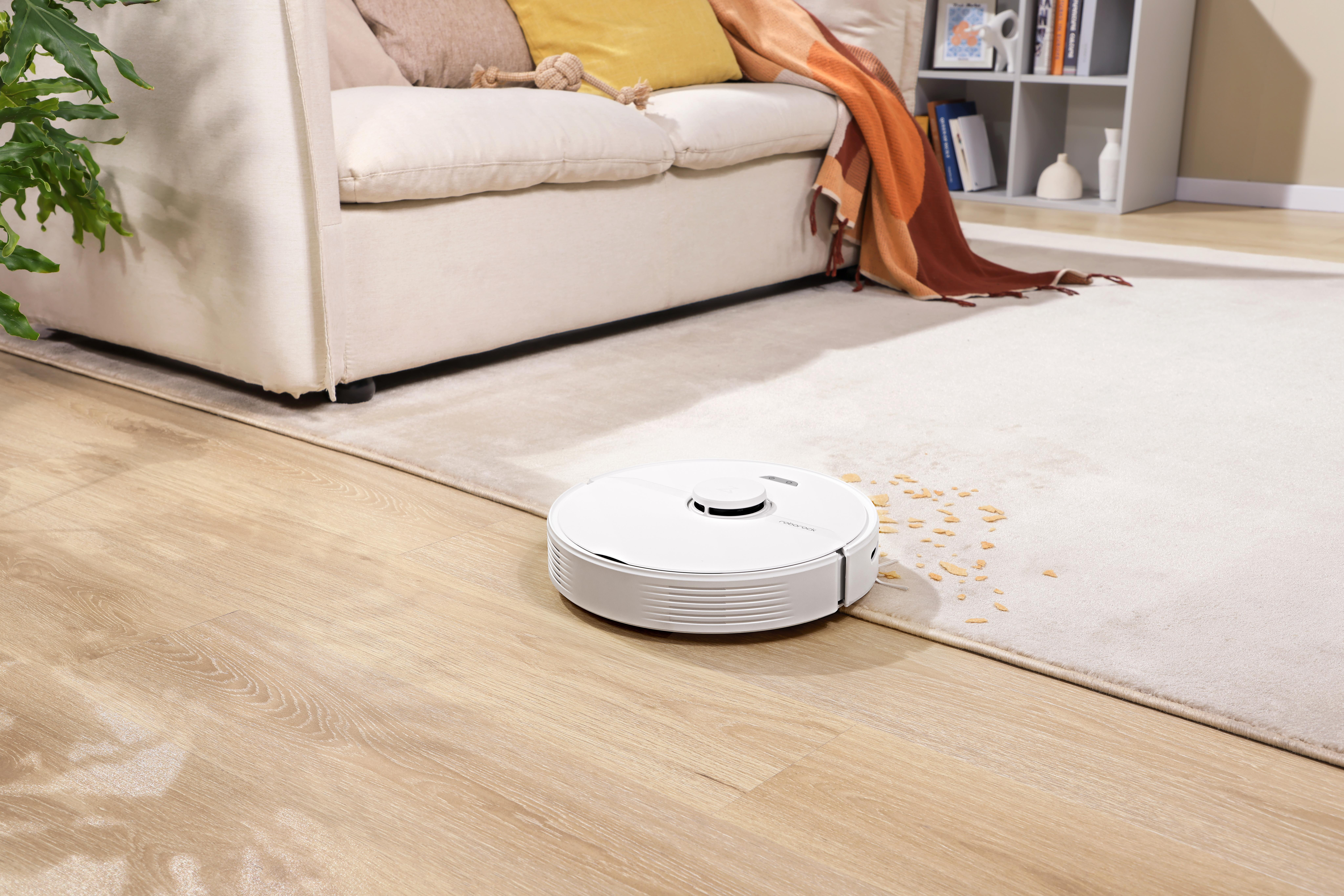 Ein weißer Roboter-Staubsauger reinigt einen hellfarbigen Teppich auf einem Holzboden.