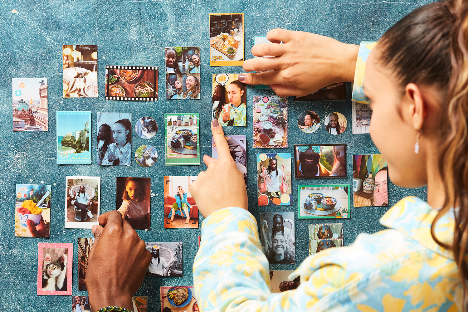Two people arranging photographs on a blue wall, featuring various images.