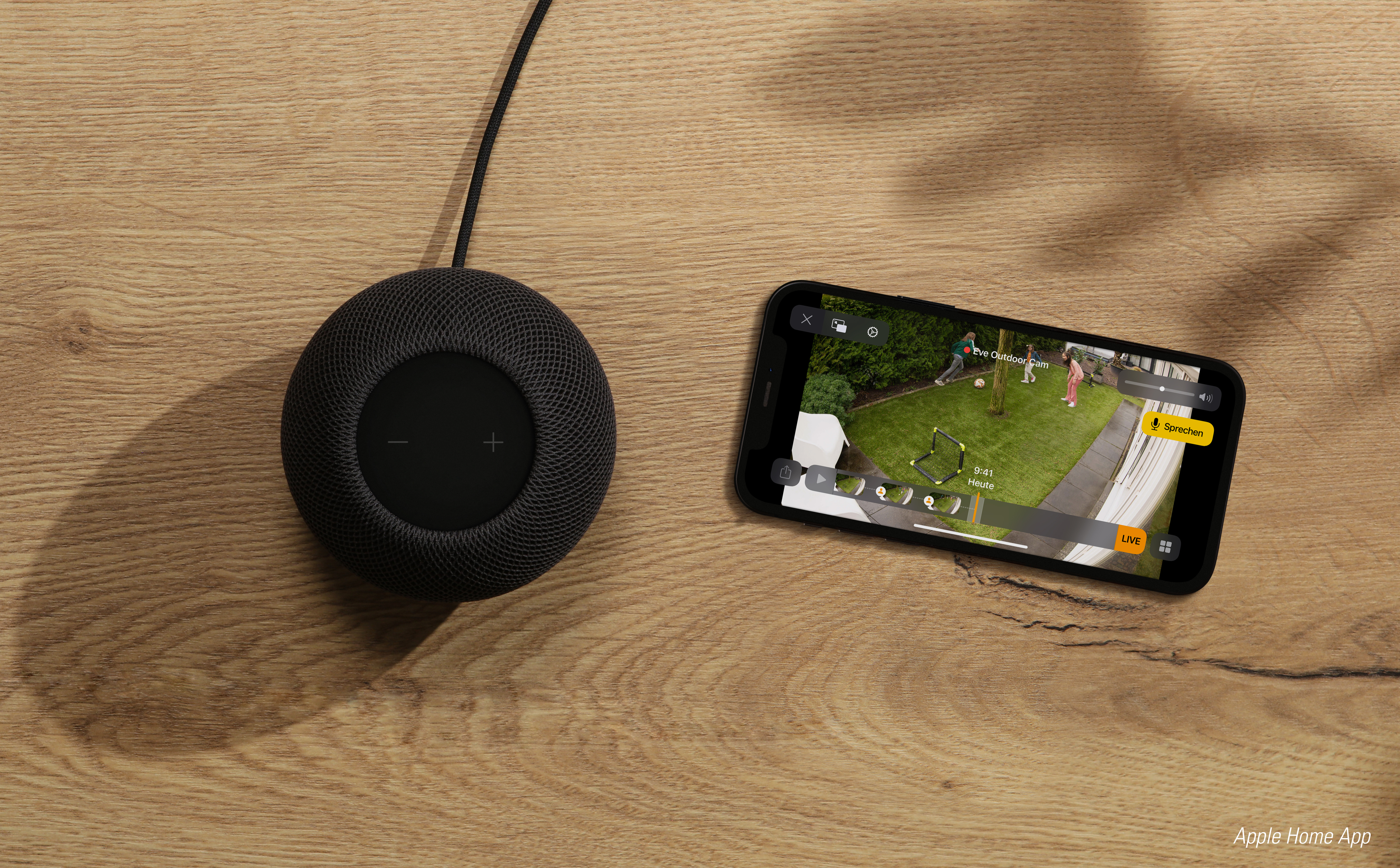 Schwarzer Lautsprecher und ein Telefon, das eine Home-Security-Kamera-Feed auf Holz zeigt.