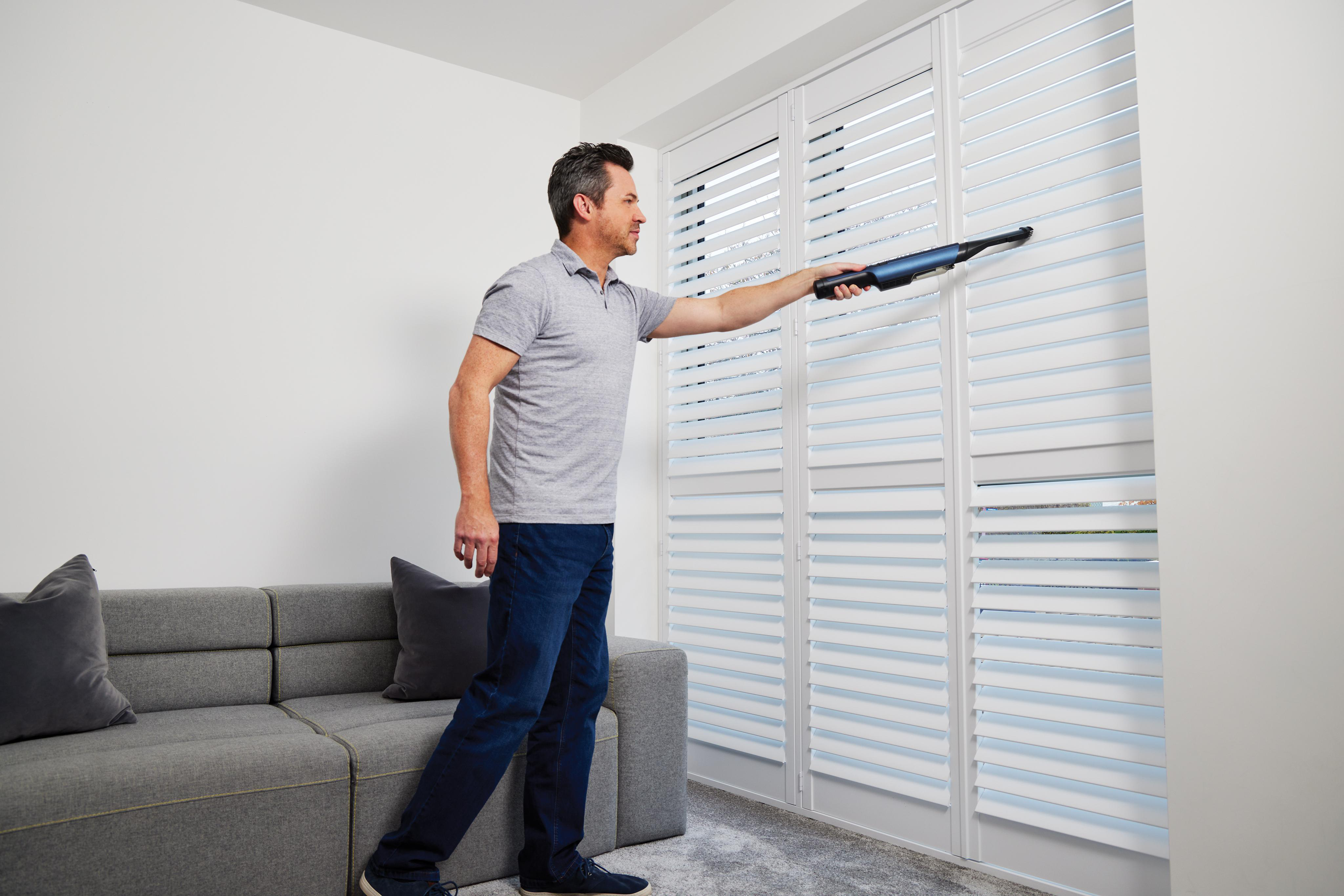 Mann, der weiße Fensterläden mit einem Handstaubsauger absaugt.