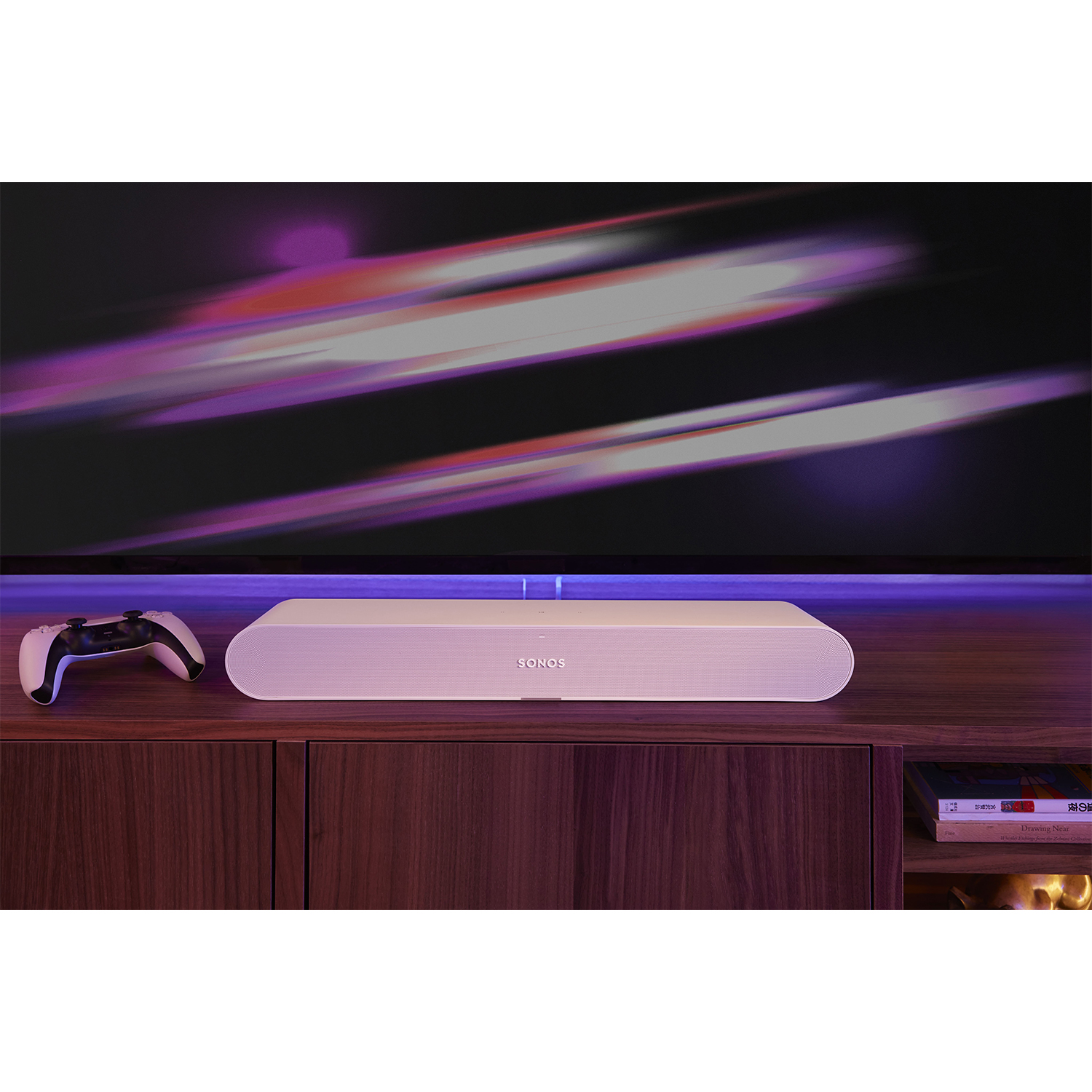 Una soundbar è su un mobile in legno sotto una TV, con un controller di gioco a sinistra.