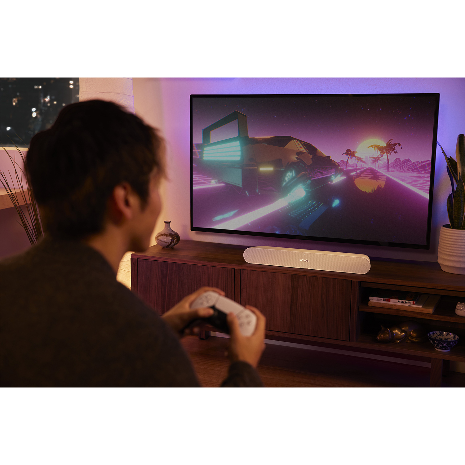 Persona che gioca a un videogioco su TV con soundbar sotto. Scena di gioco retrò sullo schermo.