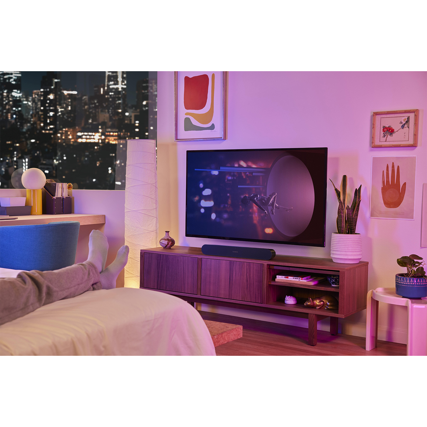 Una persona si rilassa su un letto, guardando la TV. La stanza ha arte e luci della città all'esterno.