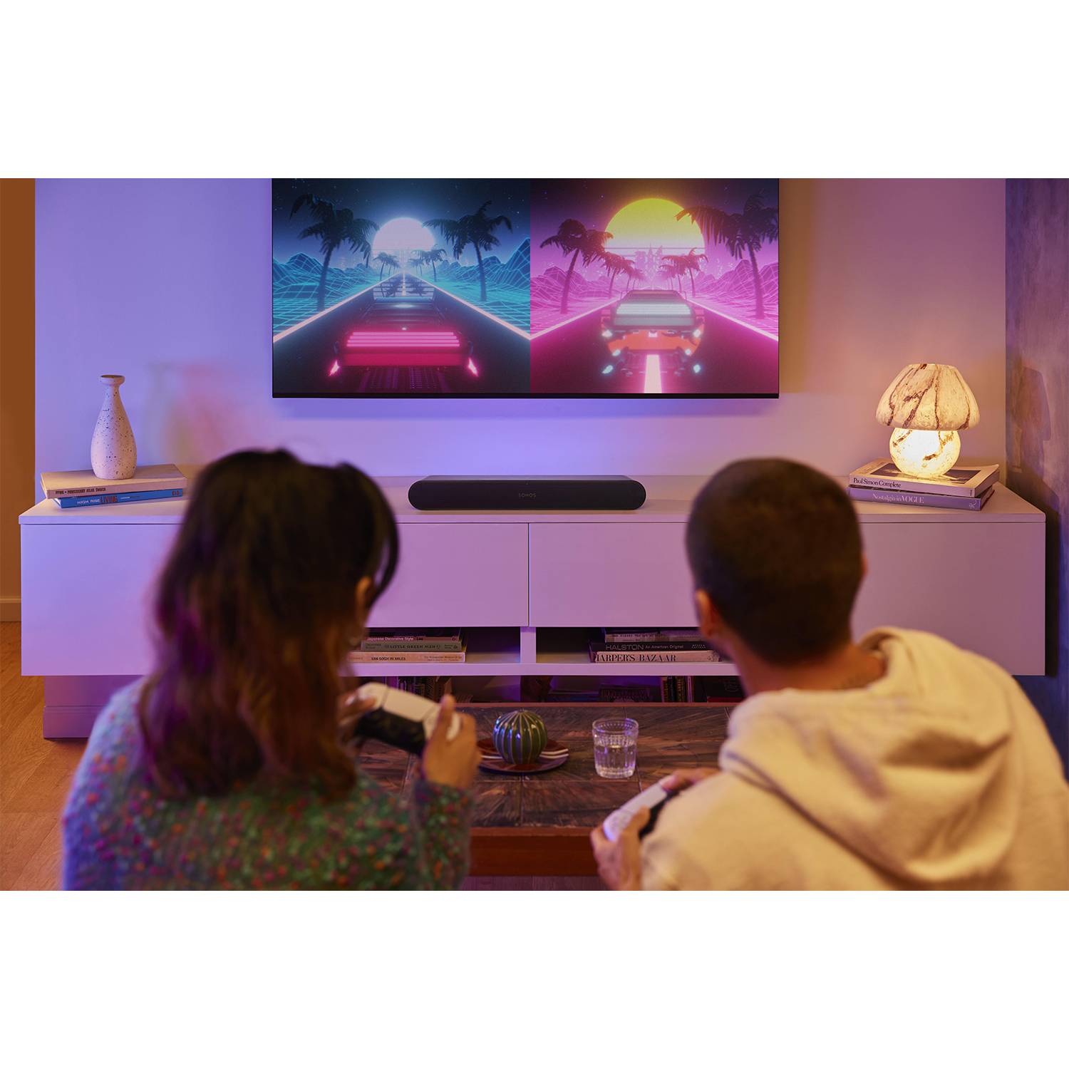 Due persone giocano ai videogiochi davanti a una TV che mostra una scena di corsa di auto al neon.