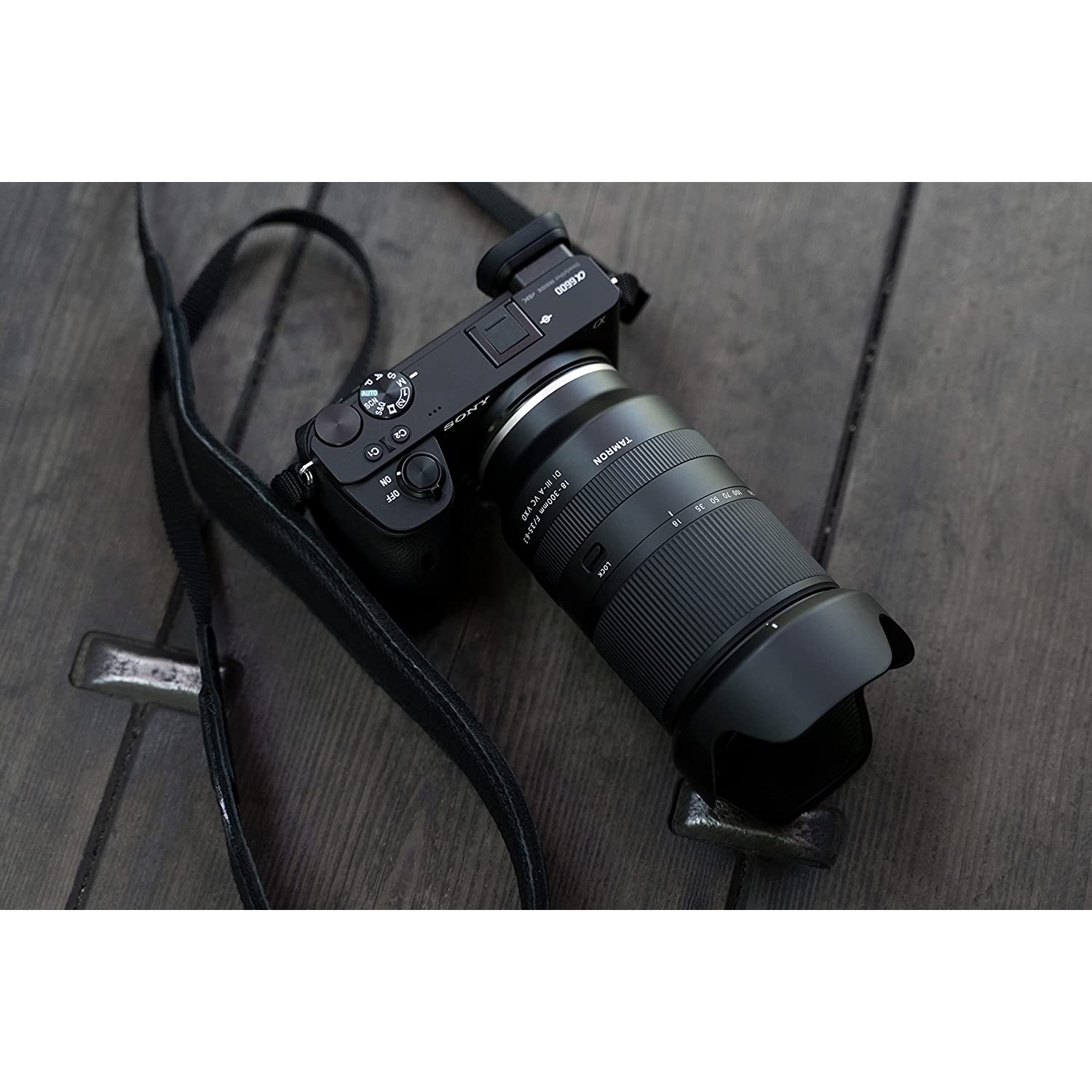 Fotocamera nera con obiettivo su una superficie di legno, con un cinturino in pelle.