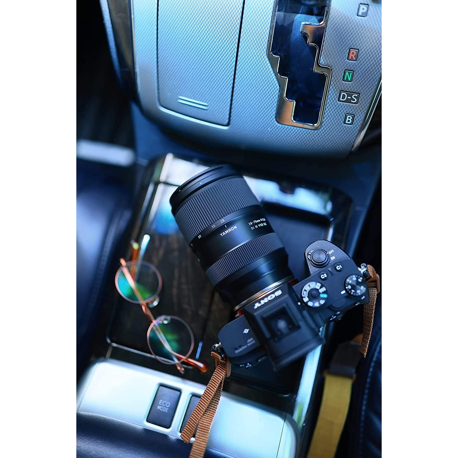 Una fotocamera e un obiettivo sulla console di un'auto accanto a occhiali da sole. Anche la leva del cambio è nell'inquadratura.