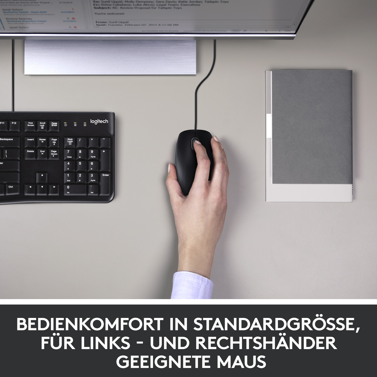 Hand auf schwarzer Maus, schwarze Tastatur und Monitor auf grauer Oberfläche.