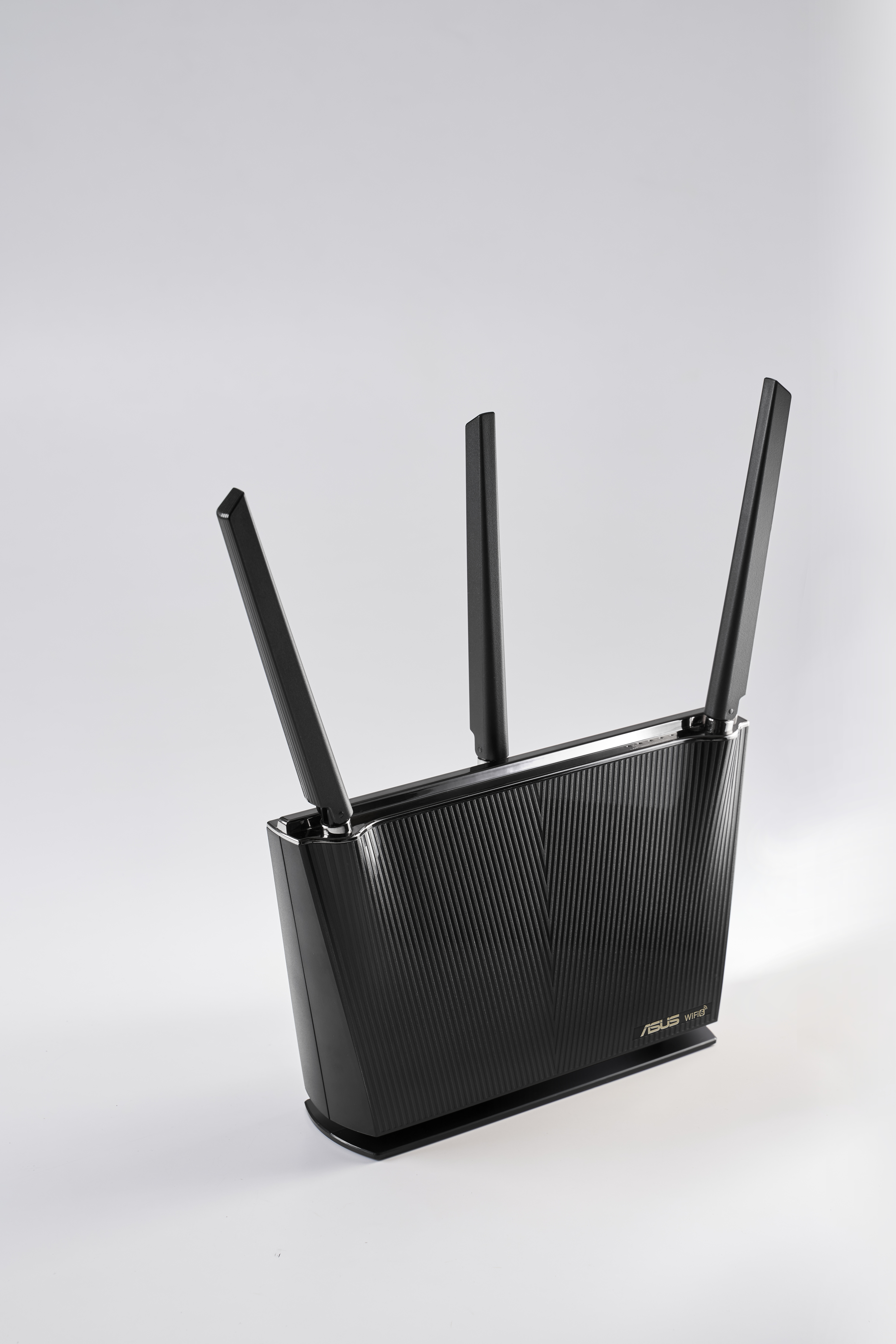 A black ASUS router with three antennas extending upwards. It sits on a white surface.