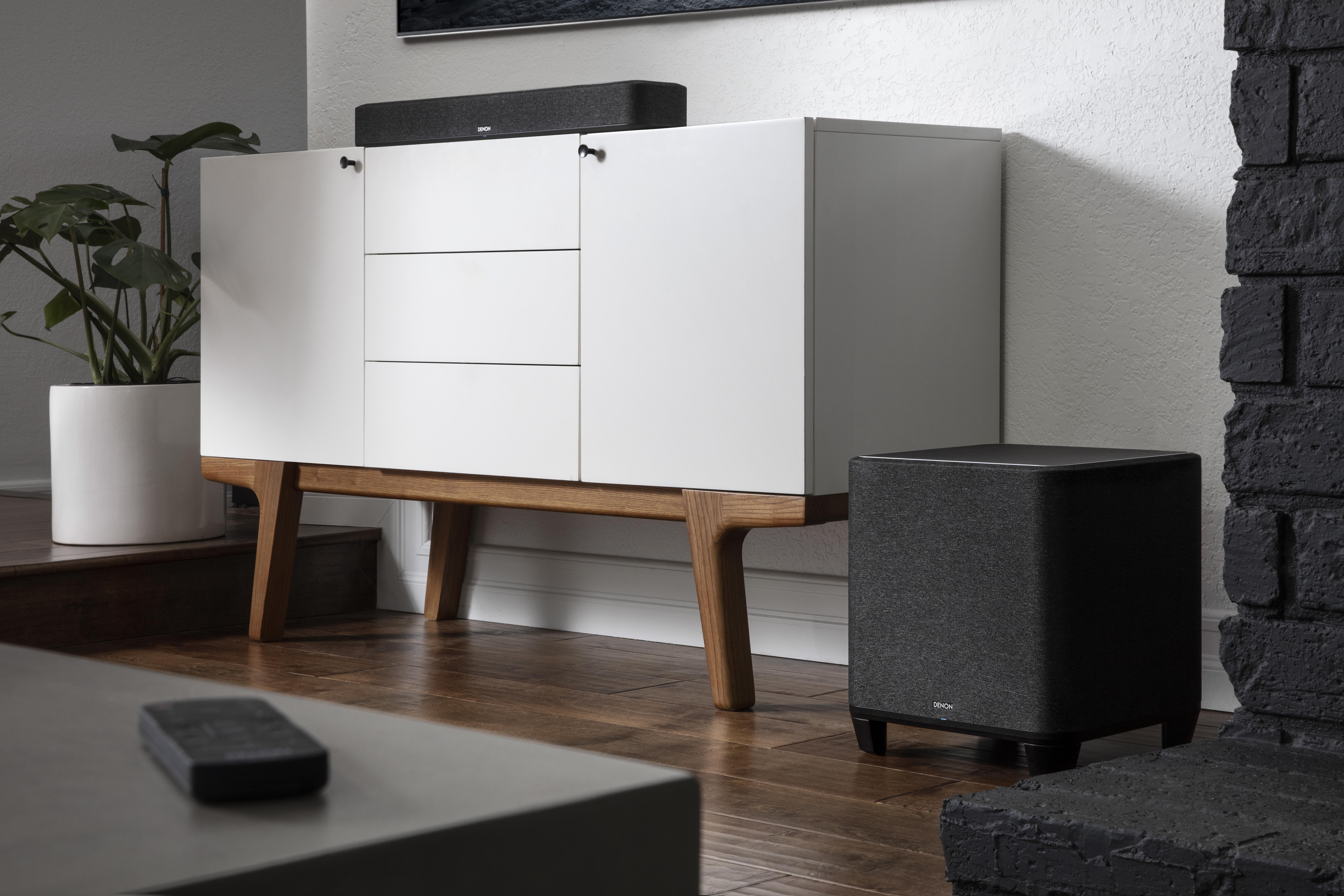 Ein weißer Schrank mit Subwoofer. Eine Soundbar befindet sich oben. Kamin rechts.