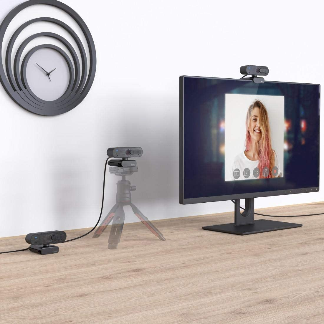 Configuración de webcam con monitor mostrando a una mujer. Reloj en la pared.