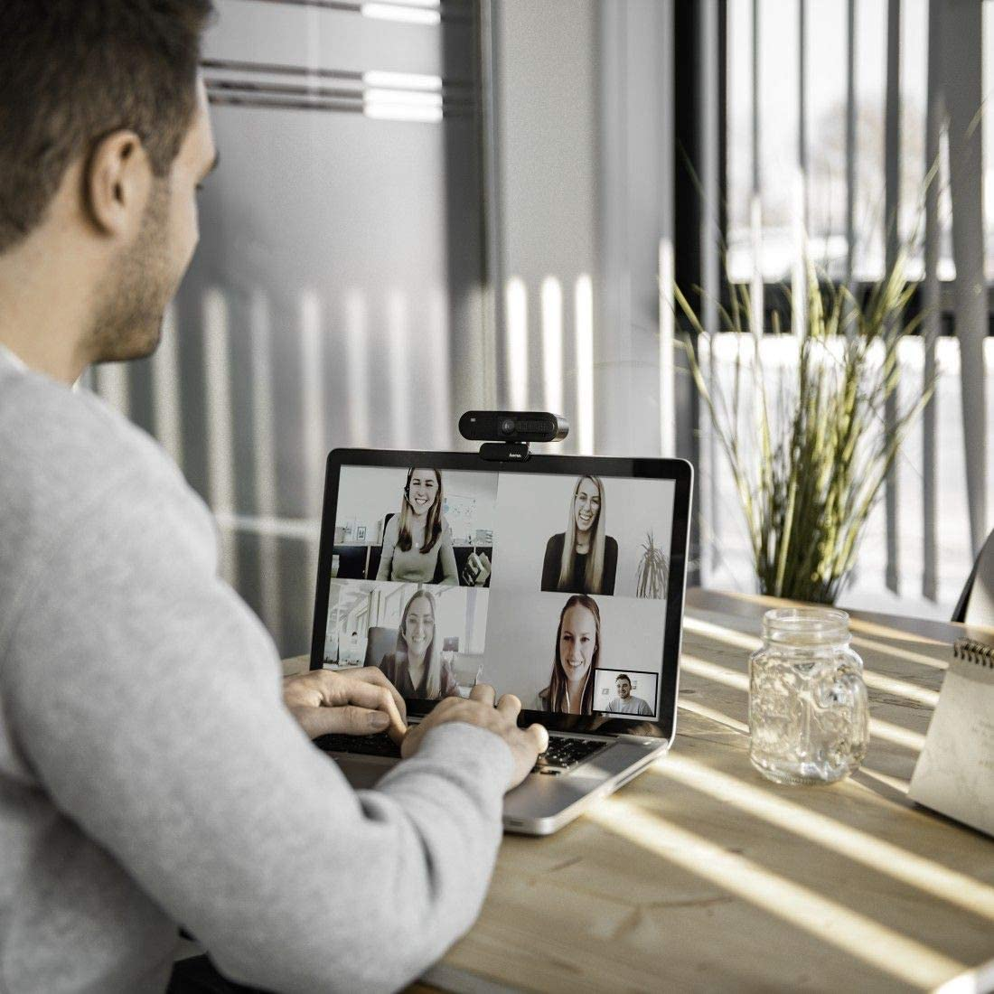Un hombre en una videollamada con cuatro personas en una pantalla de portátil, webcam arriba.
