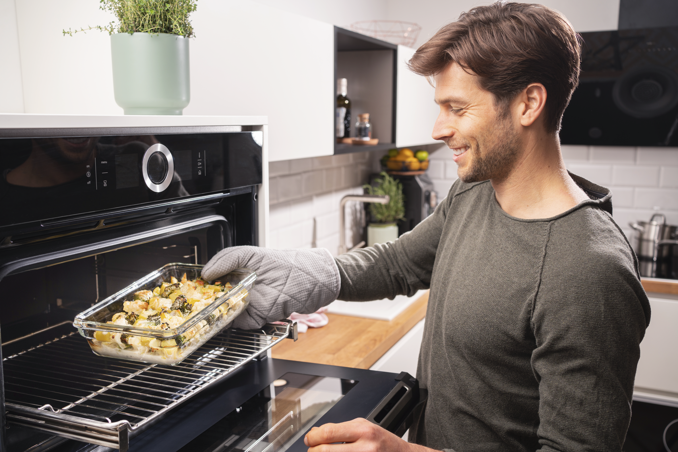 Un hombre sonriendo, sacando una fuente de horno de un horno en una cocina.
