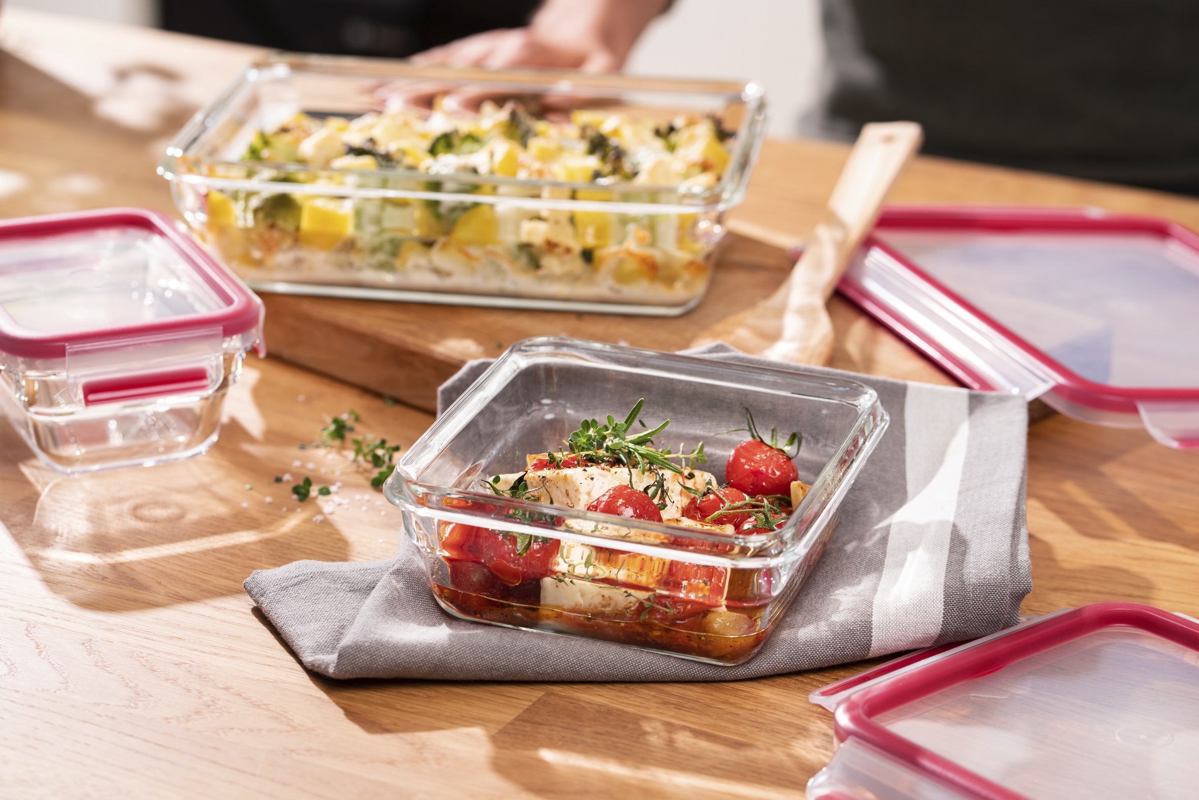 Recipientes de vidrio con comida, incluyendo platos horneados con verduras y un plato con tomates.