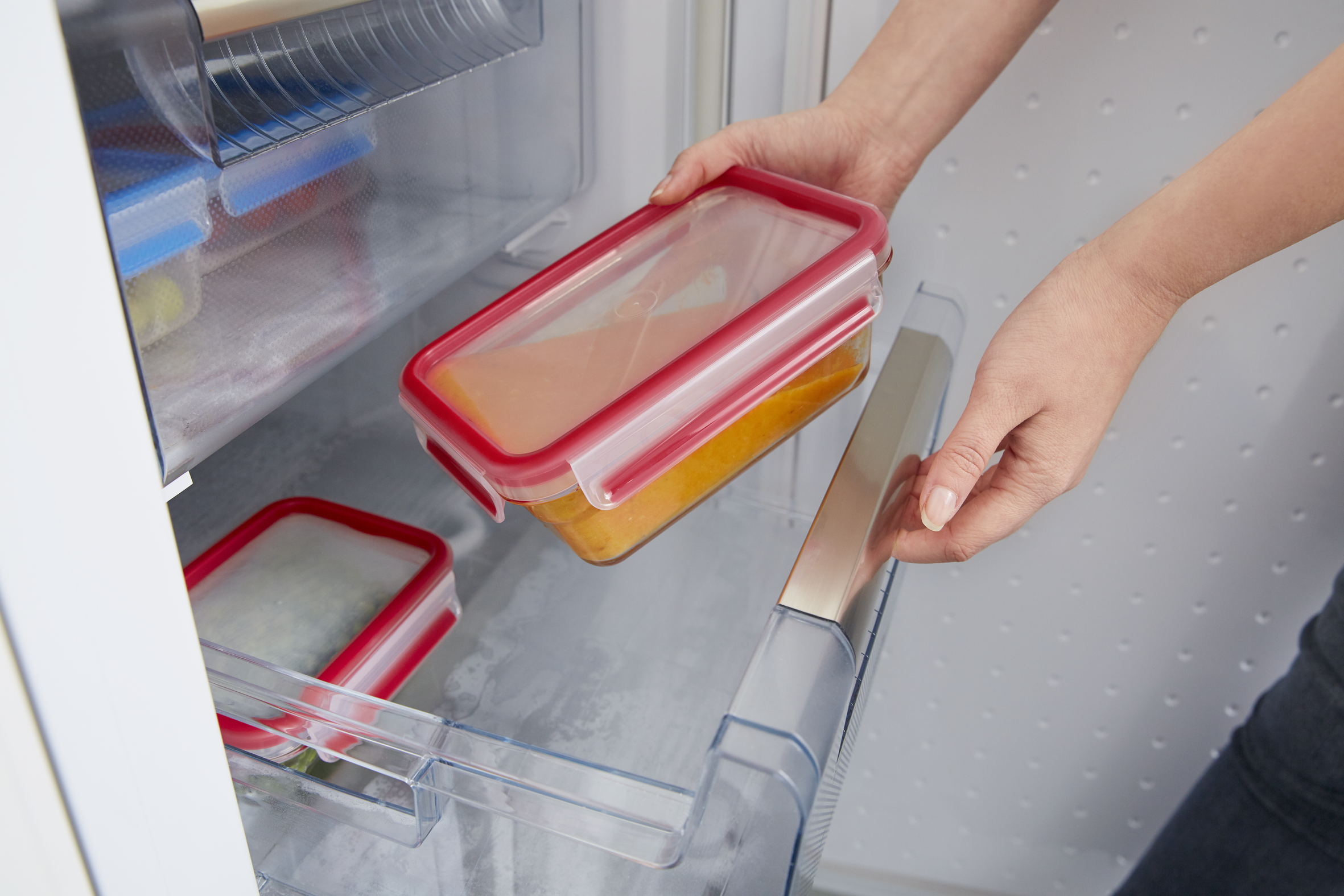 Manos colocando un recipiente con comida en un refrigerador.
