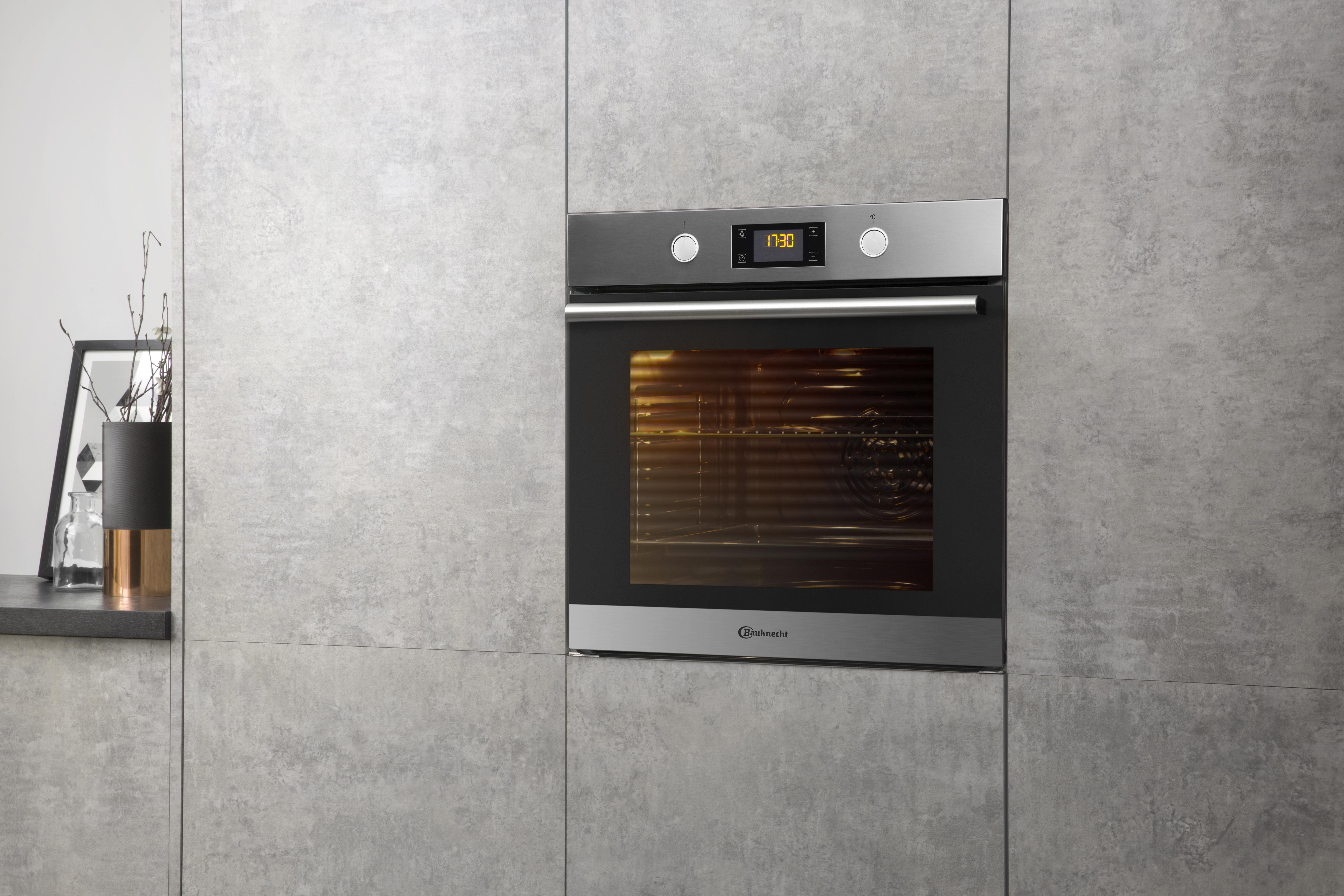 Einbau-Backofen in einer grauen Küche. Ofen ist Edelstahl. Digitalanzeige zeigt die Zeit. Neutraler grauer Hintergrund.