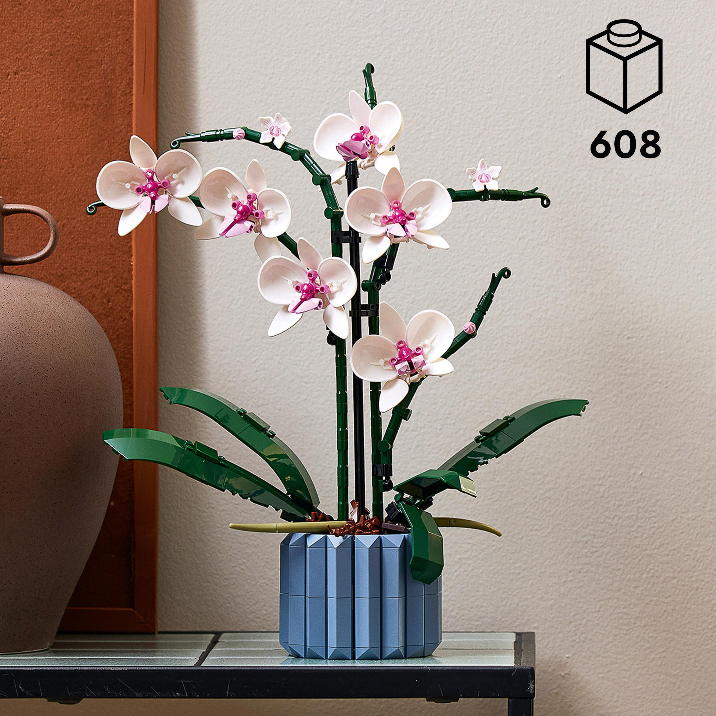 LEGO Orchideenpflanze mit weißen und rosa Blüten in einem blauen Topf auf einem Glastisch.