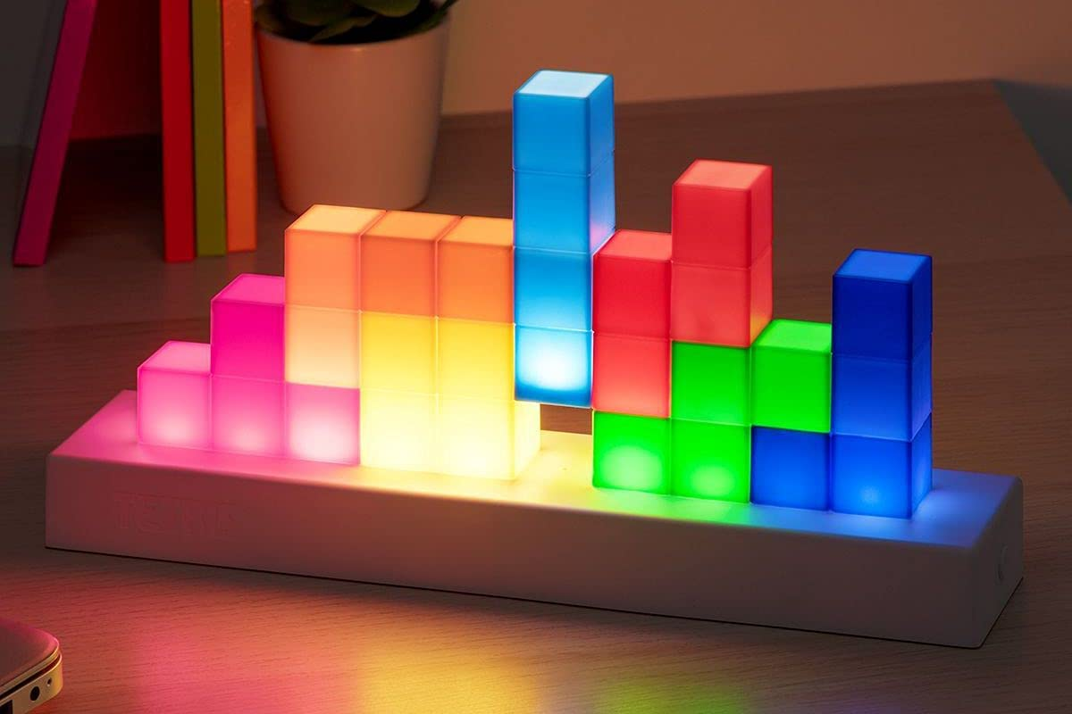 Egy világító Tetris-blokk lámpa fehér alappal. A blokkok különböző színekben pompáznak, fényt mintázva.