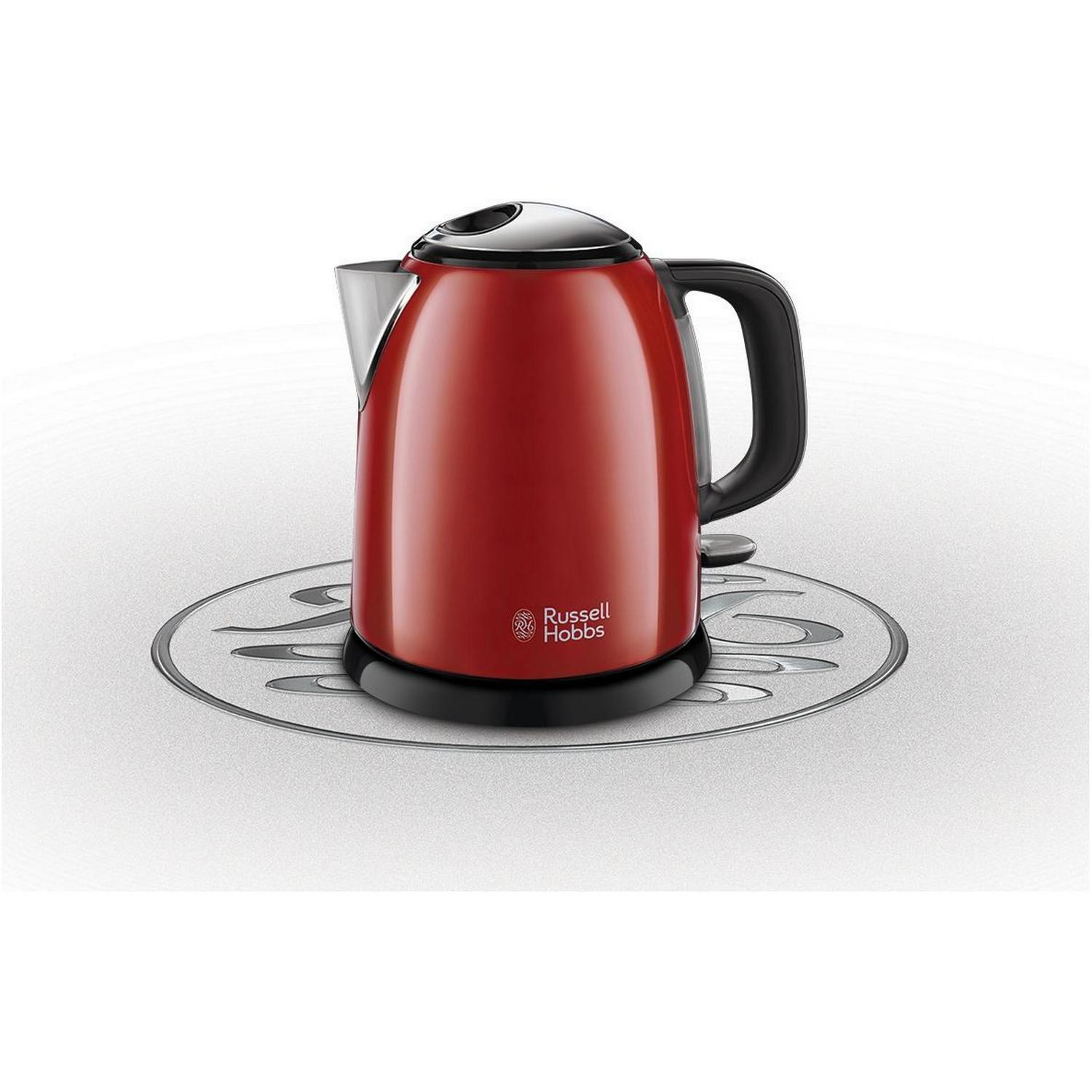 Una tetera eléctrica roja con base y asa negra, sobre una alfombra circular.