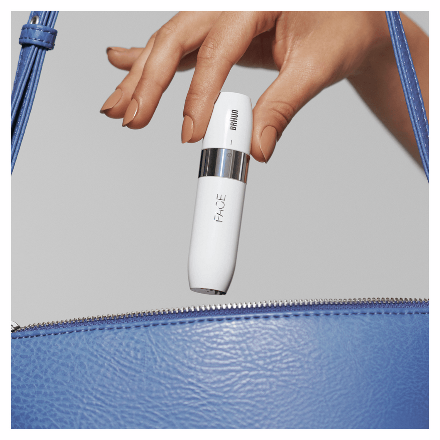 Una mano de mujer sosteniendo un dispositivo blanco para la depilación facial sobre un bolso azul.