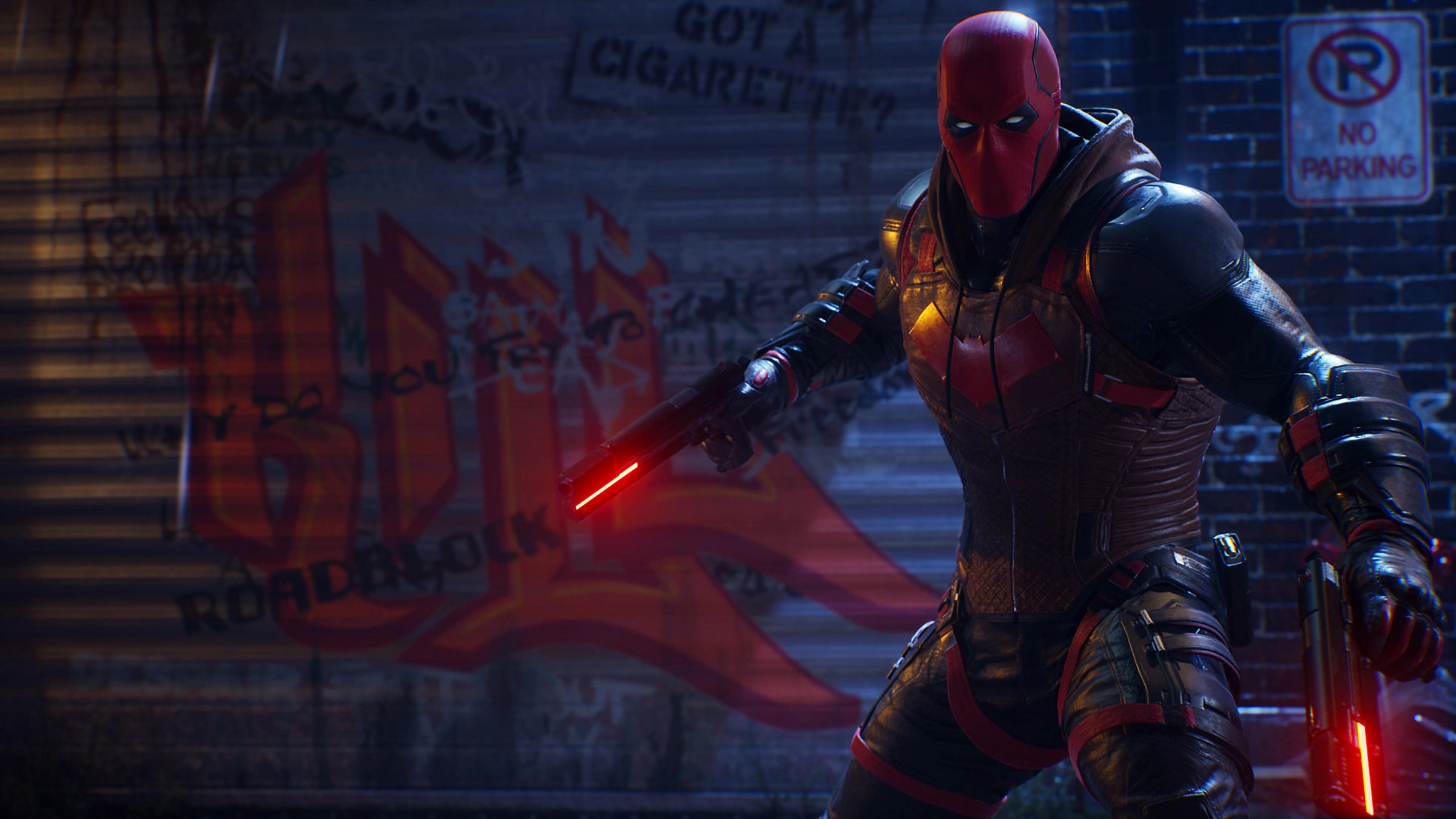 Red Hood aus Gotham Knights, mit zwei Waffen, vor einer graffiti-bedeckten Backsteinmauer.