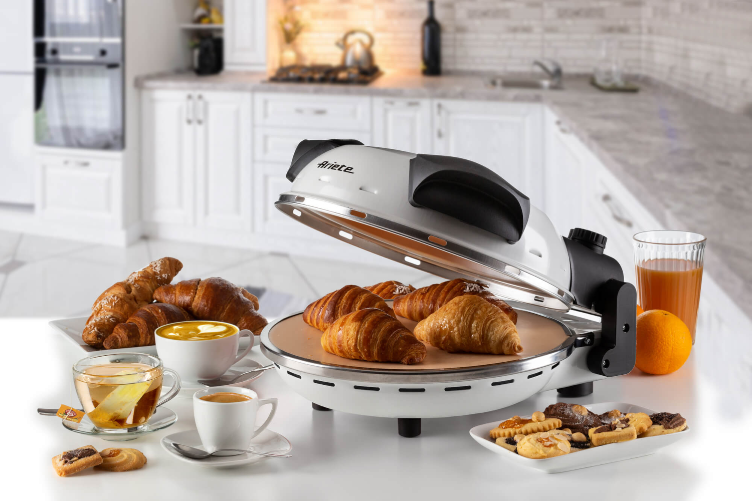 Fehér pizzakemence croissant-okkal, kávéval, lével és péksüteményekkel az asztalon.