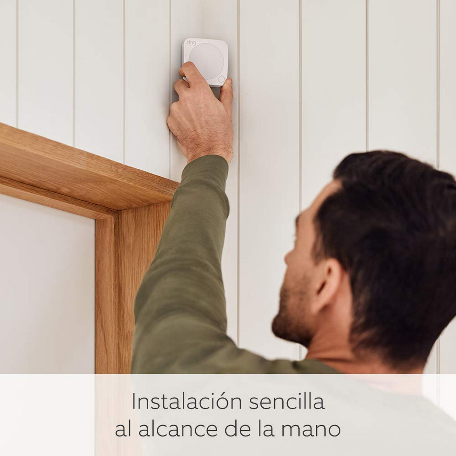 Hombre instalando un sistema de alarma Ring blanco en una pared blanca, junto a un marco de puerta de madera.