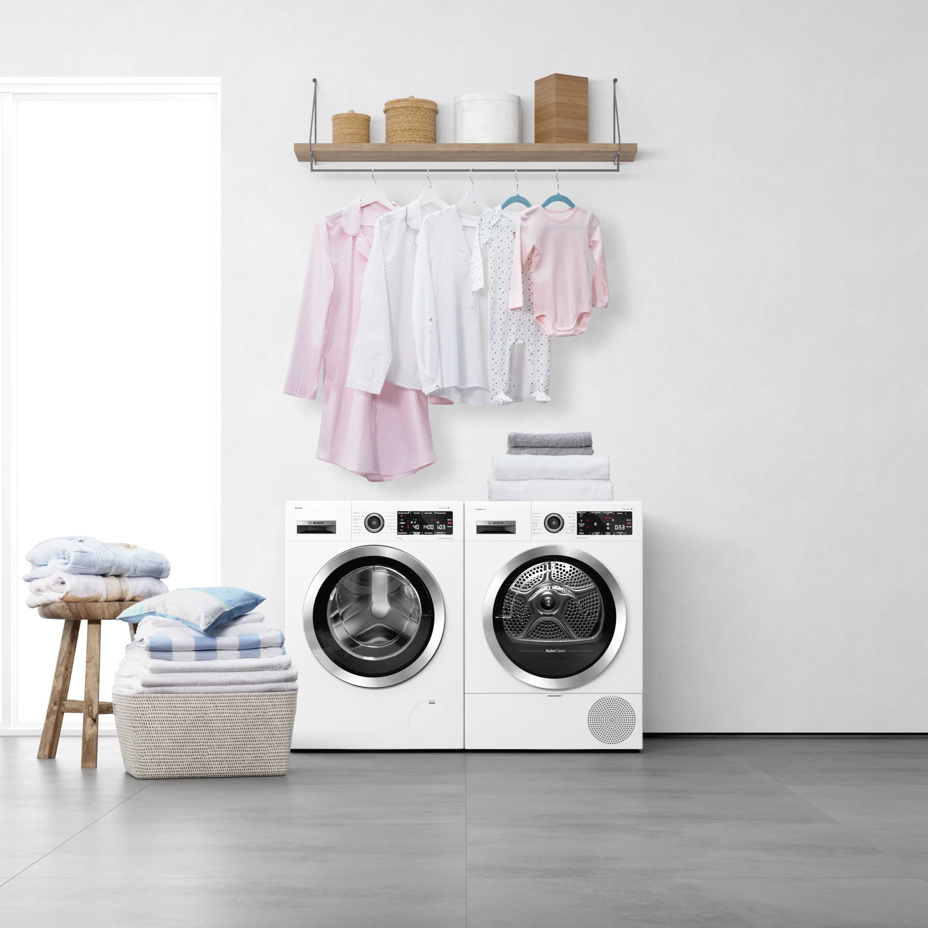 Witte wasmachine en droger met opgevouwen kleren en babykleding erboven.
