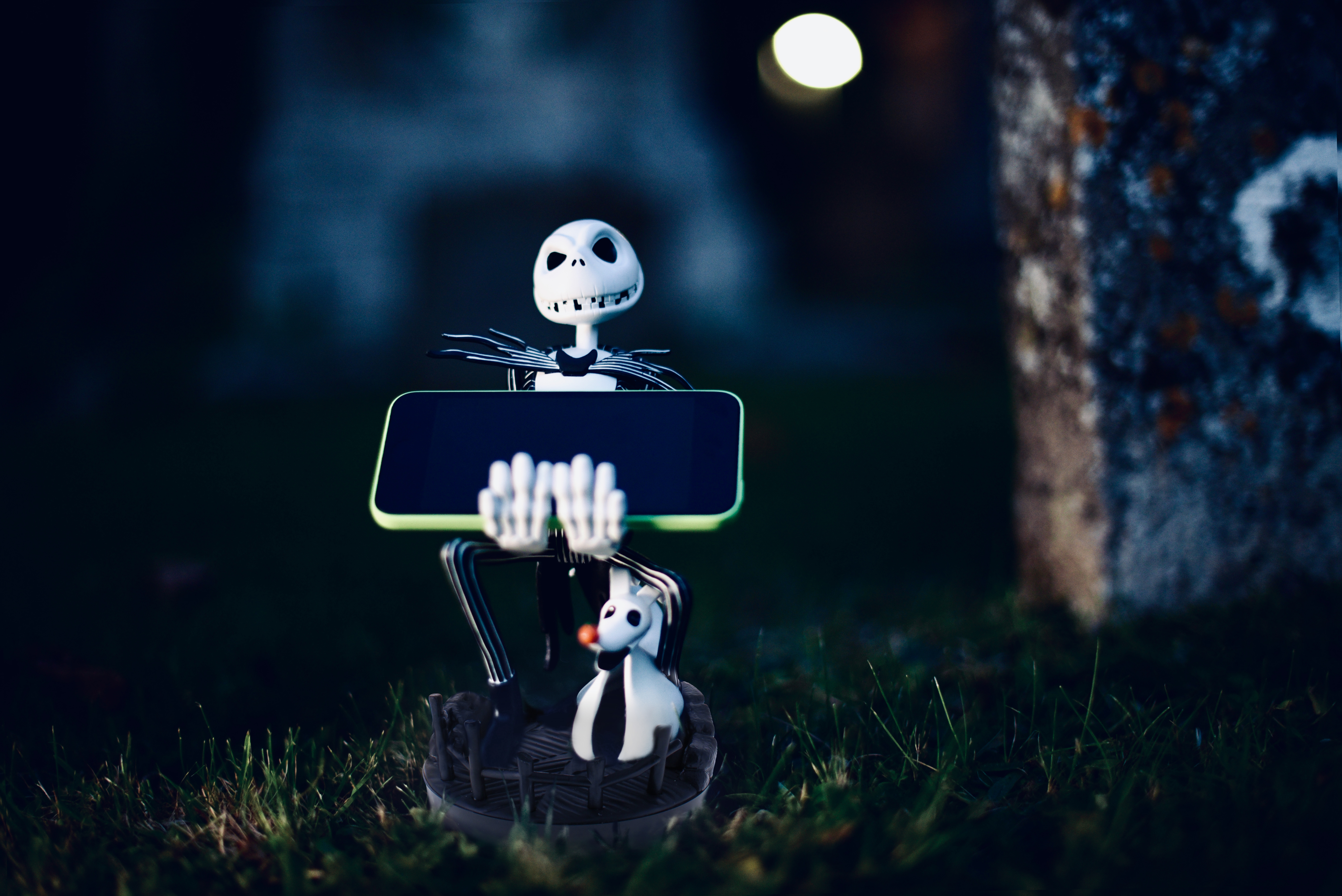 Una figura di Jack Skellington che tiene un telefono, in una scena spettrale di cimitero di notte.
