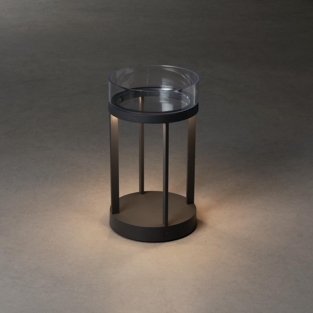 Schwarze zylindrische Lampe. Es hat eine Glasplatte und wird von unten beleuchtet, auf einer grauen Oberfläche.