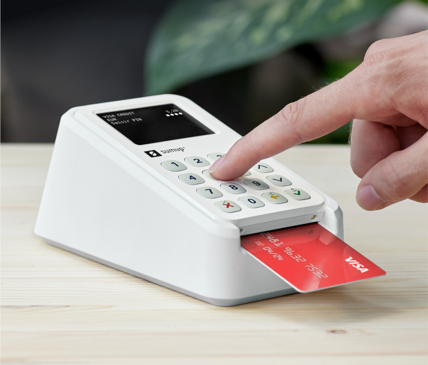 Une main appuie sur un bouton sur un terminal de paiement blanc, une carte de crédit est insérée.