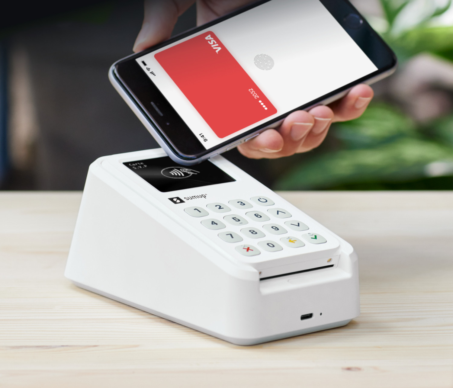 Un téléphone est tenu au-dessus d'un lecteur de carte blanc, montrant une carte VISA rouge.