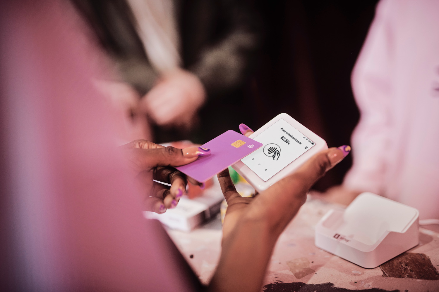 Une personne tenant une carte de crédit au-dessus d'un terminal de paiement, une carte violette.