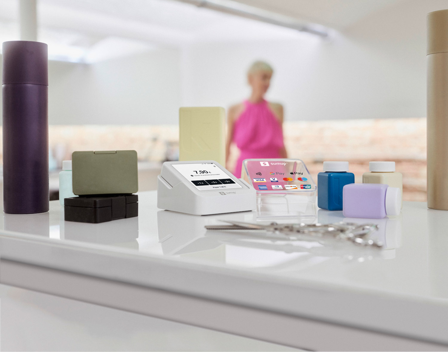 Terminaux de paiement et accessoires sur une surface blanche, avec une personne floue en arrière-plan.
