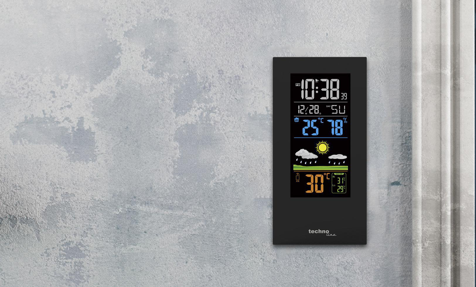 Schwarze Wetterstation. Zeigt Uhrzeit, Temperatur, Luftfeuchtigkeit und Wettersymbole an einer Wand.