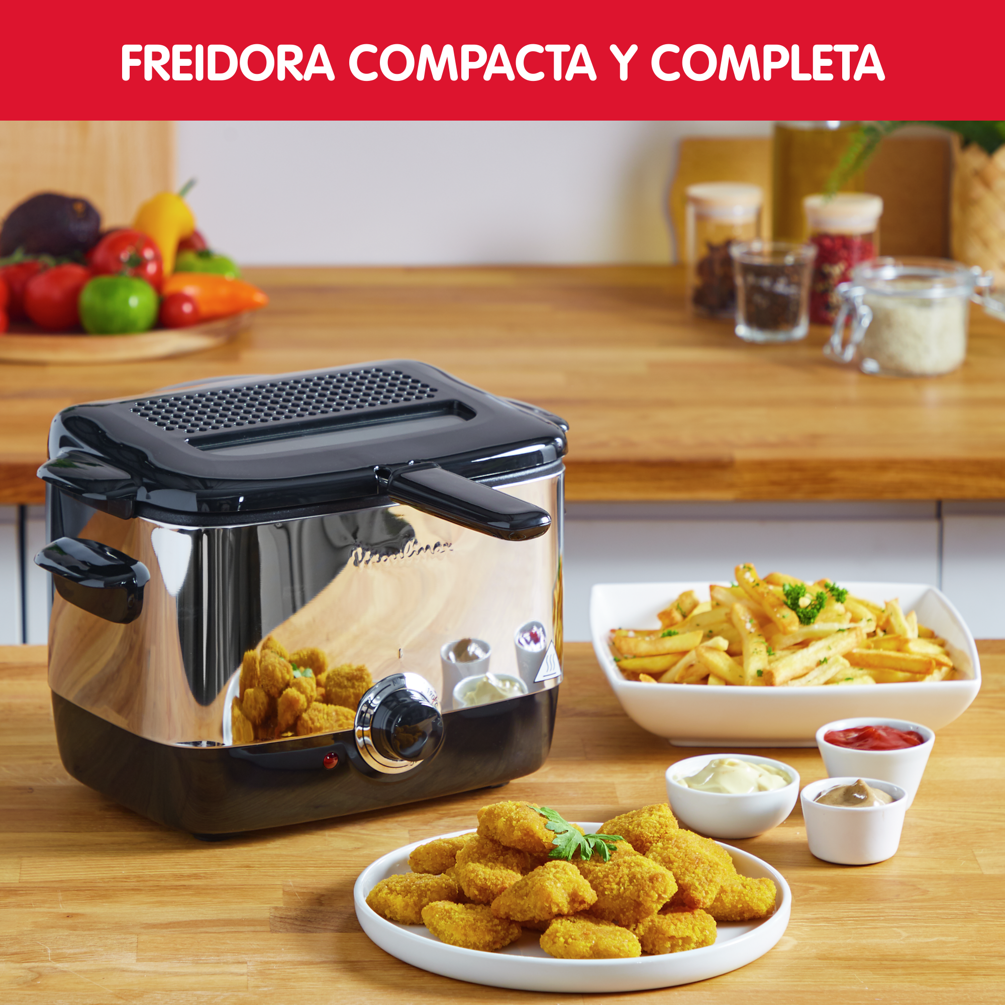 Freidora Moulinex con nuggets y patatas fritas. Tres pequeños cuencos de salsas, en una encimera de madera.