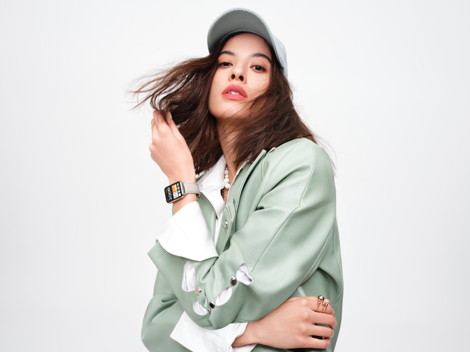 Une femme avec un chapeau et une veste verte porte une montre connectée, regardant la caméra.